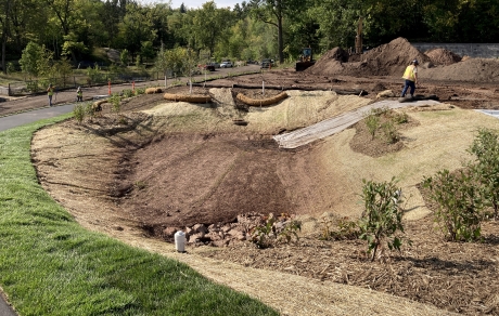 Tan erosion control material lines a basin ringed by mulched shrubs and a paved trail
